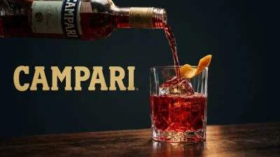 Campari rosso intenso versato in un bicchiere con ghiaccio e riflessi luminosi in un’atmosfera elegante