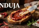 Nduja calabrese spalmata su pane rustico con consistenza morbida e colore rosso intenso leggermente oleoso