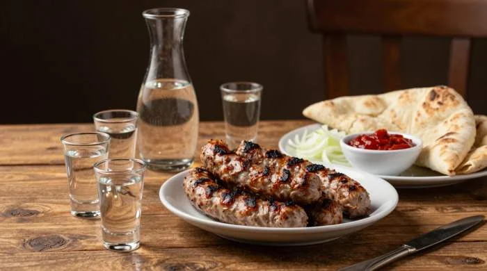 Bicchieri di rakia serviti accanto a ćevapi balcanici