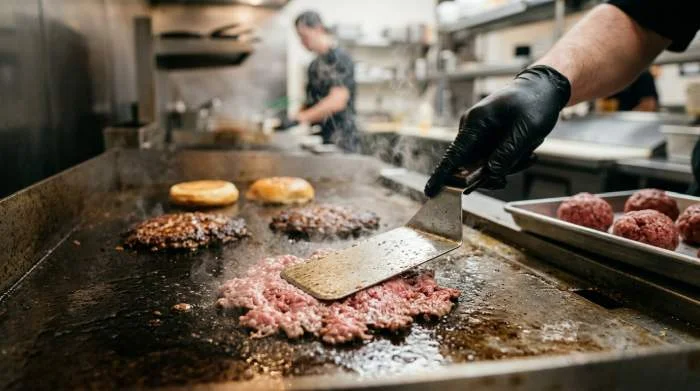 Smash burger preparato su piastra calda con carne schiacciata e crosta croccante